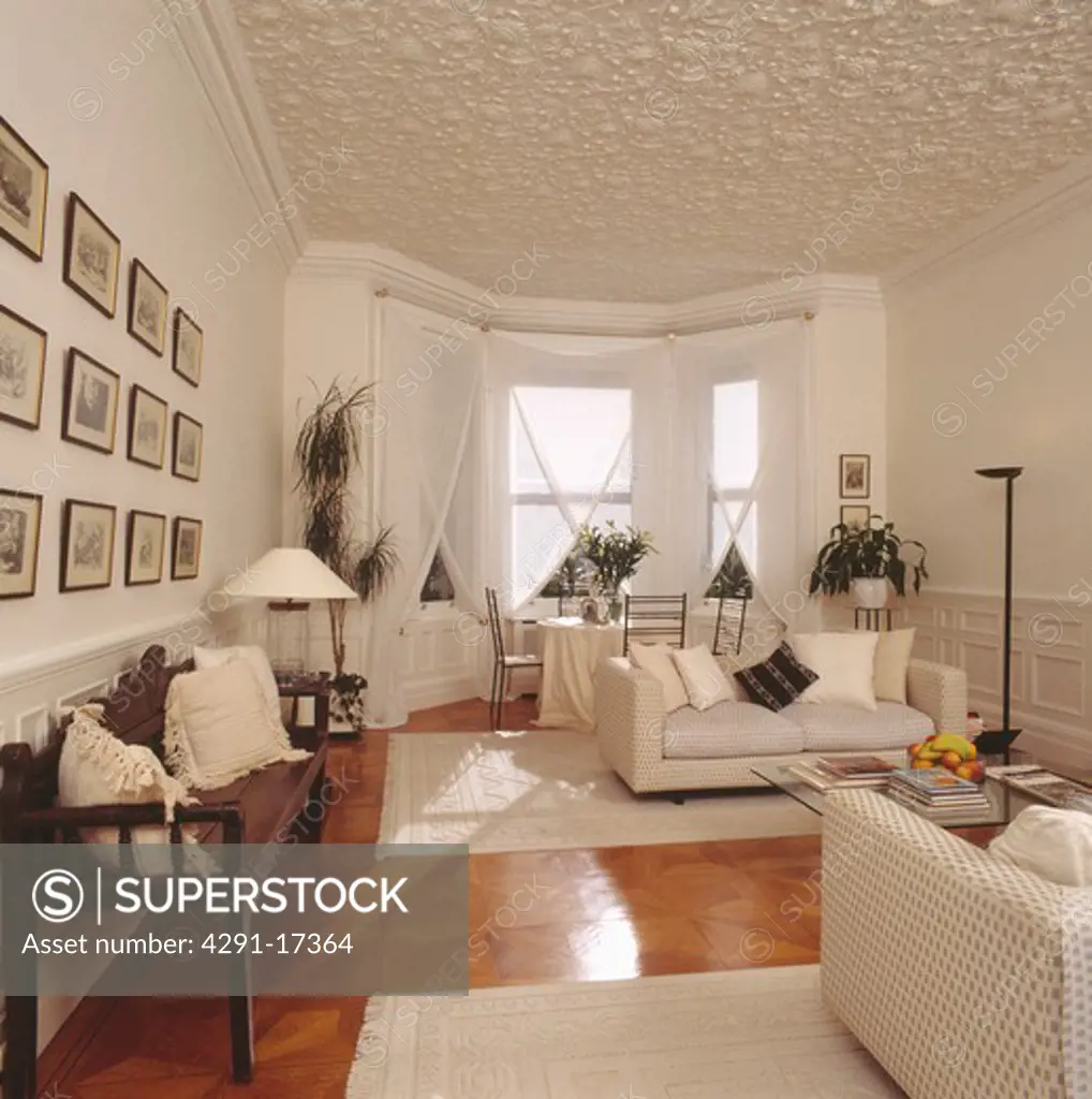 Textured ceiling in white living room with wooden settle and white sofas & cream rugs on polished wooden flooring