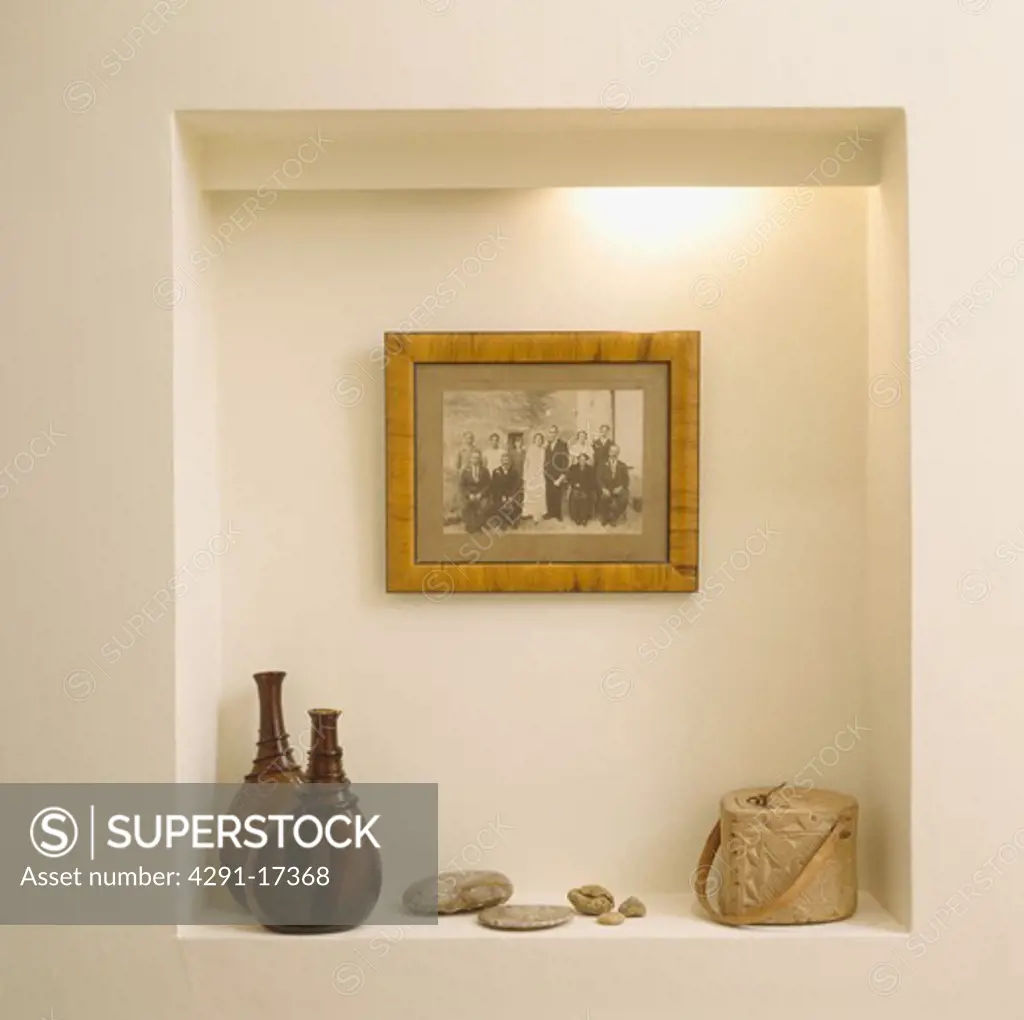 Old black & white photograph above brown glass bottles and soapstone pot in lighted alcove
