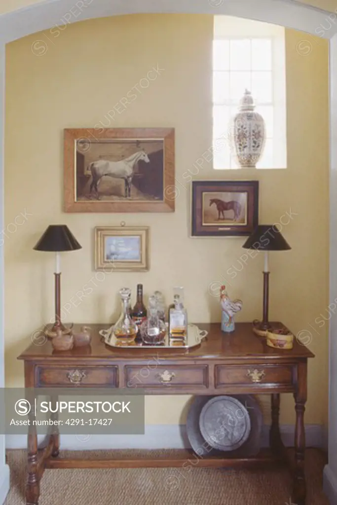 Pictures above lamps and drinks tray on antique table in diningroom alcove