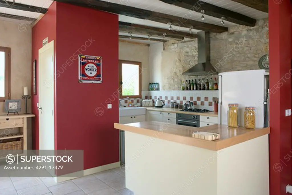 Modern kitchen in stone building with neutral coloured materials and beamed ceiling. Modern kitchen in stone building with neutral coloured materials and beamed ceiling with red feature wall.