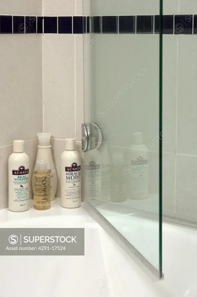 Close-up of toiletries on bath with glass shower door