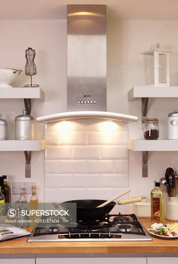 Close-up of stainless steel extractor with downlighting above wok on stainless steel gas hob