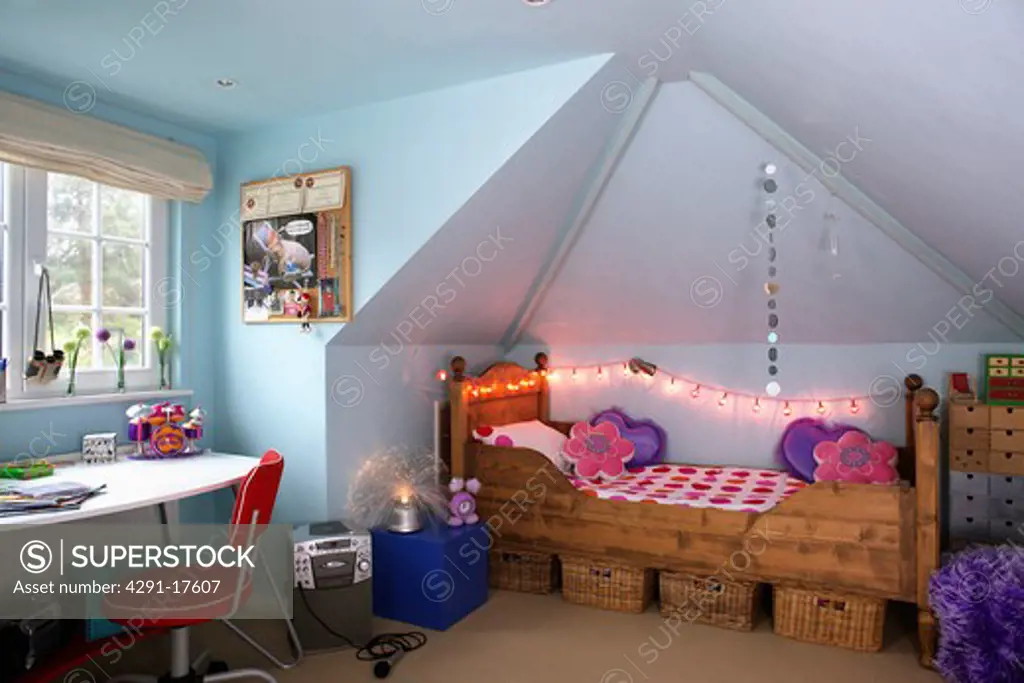 Novelty fairy lights above wooden bed in teenager's attic bedroom