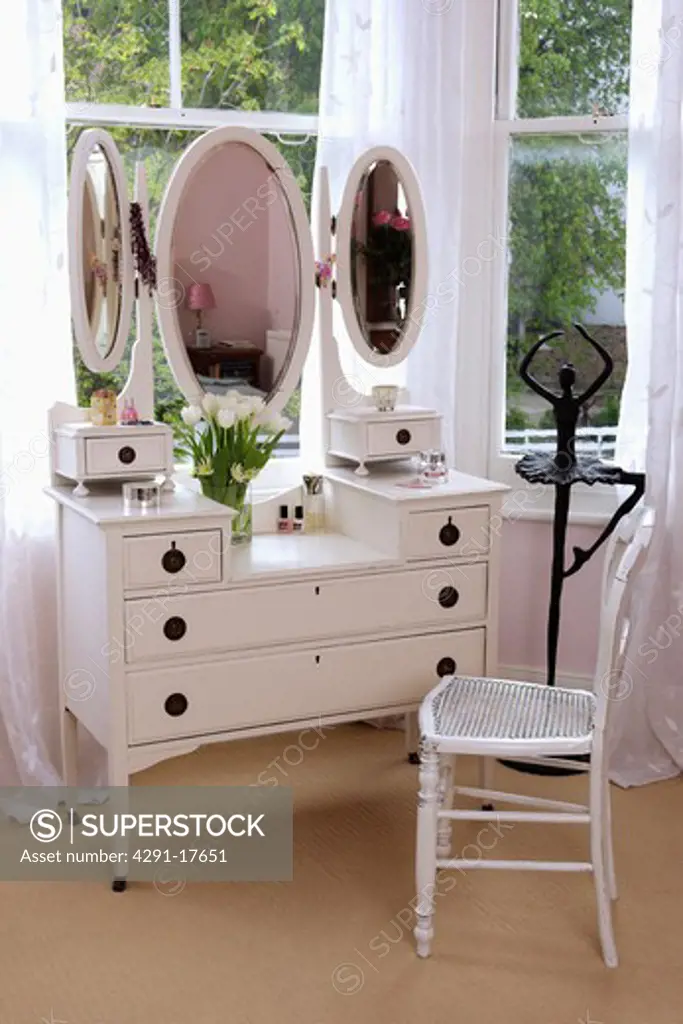 Painted white chair beside shite dressing-table with triple mirrors in front of window