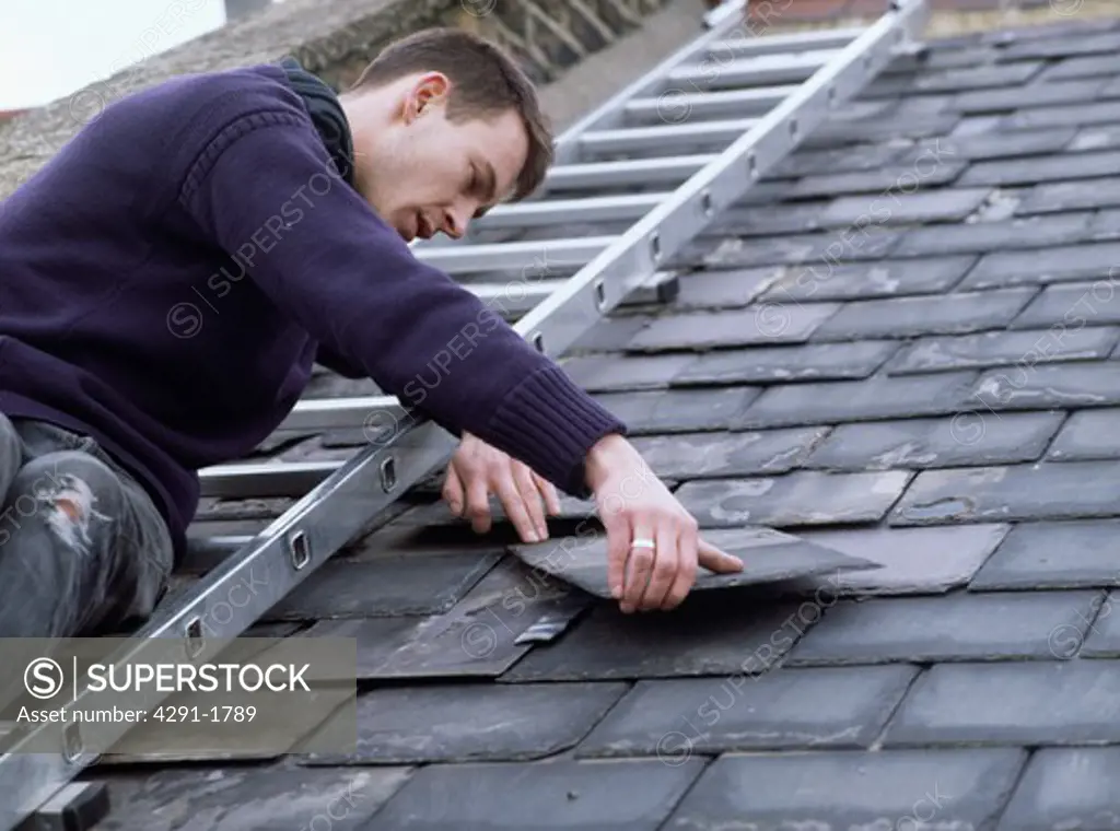 Man on ladder replacing roof slate