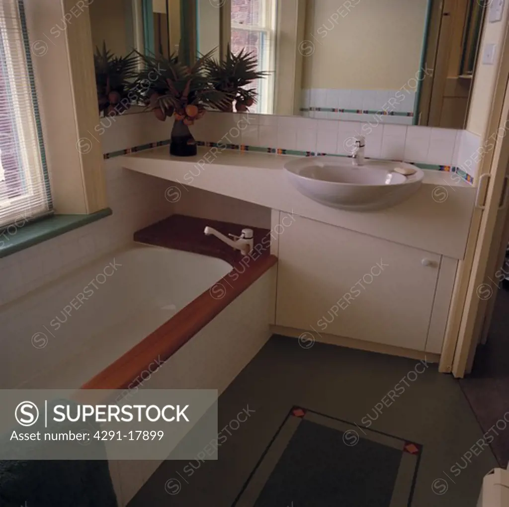 Corner tap on bath set into vanity unit with whtie basin in modern bathroom
