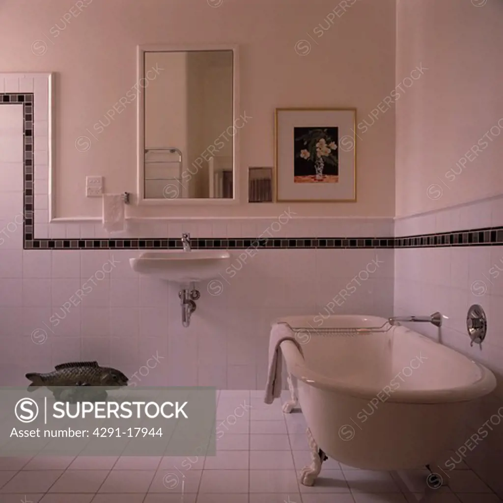 White clawfoot bath in white bathroom with white tiled wall and black border to dado height