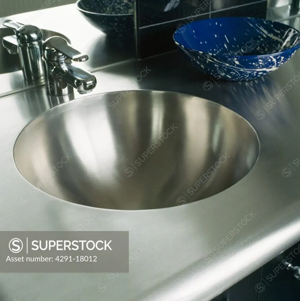 Close-up of steel tap and circular steel sink and worktop
