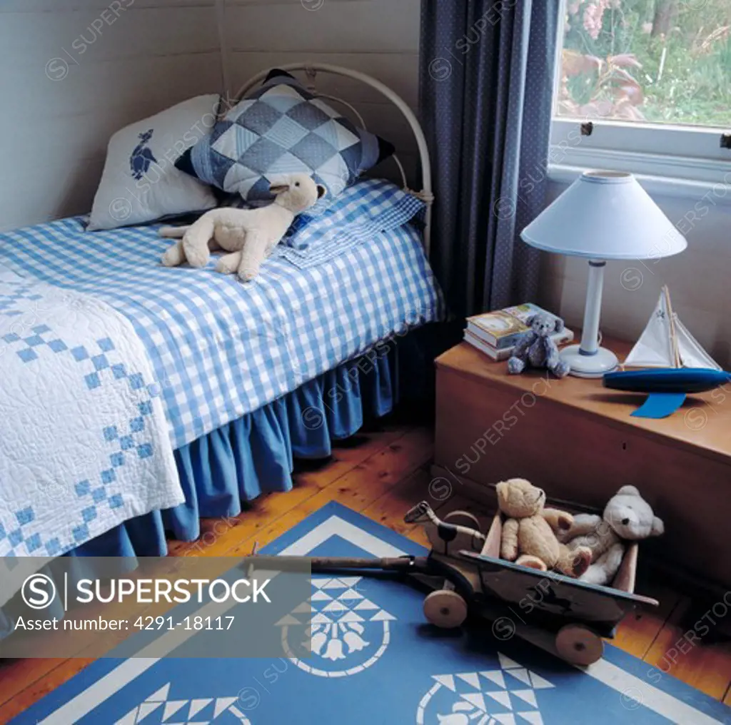 Patchwork cushions and quilt on bed with blue checked duvet in child's bedroom with blue rug and vintage toys