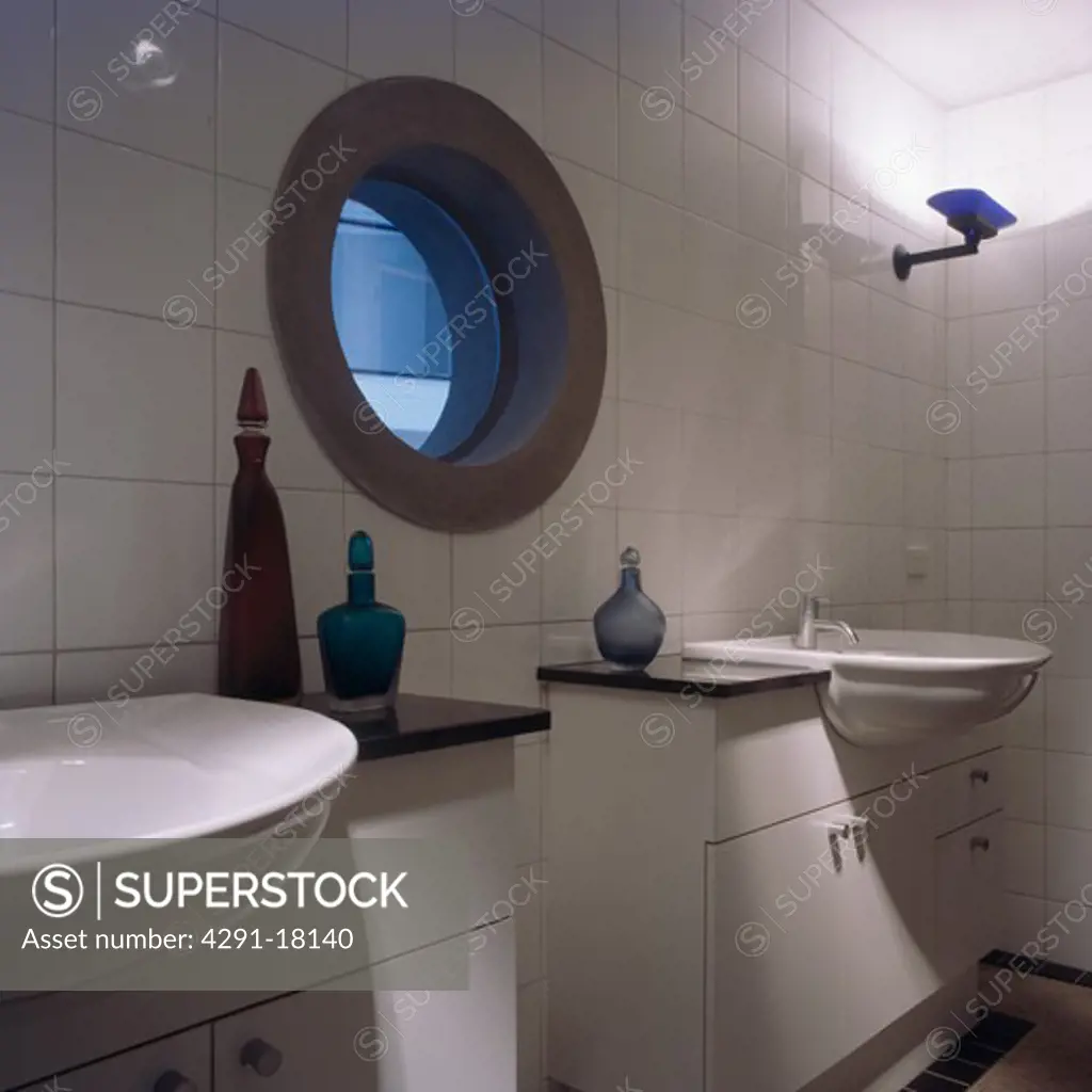 Circular window in modern white tiled bathroom with double basins