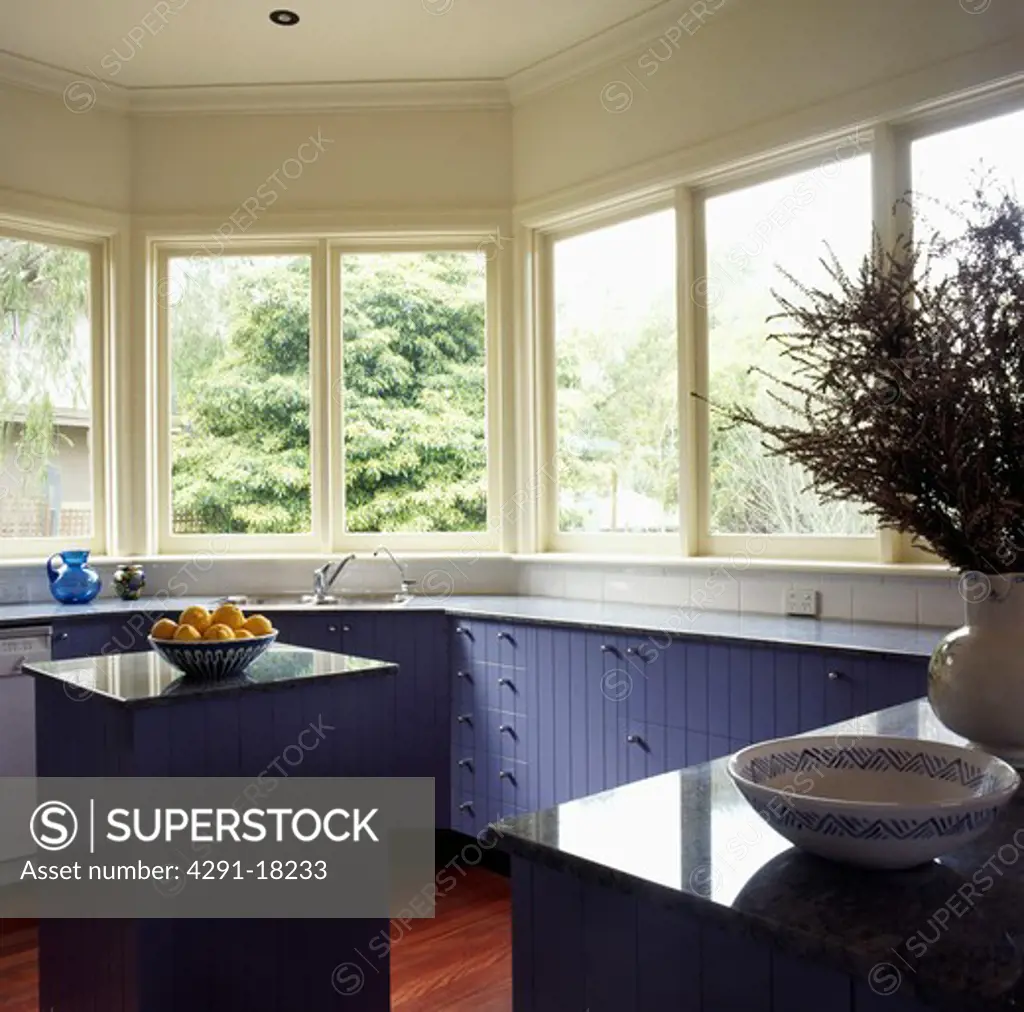 Bowl of fruit on island unit in modern white kitchen with mauve fitted cupbaords below windows