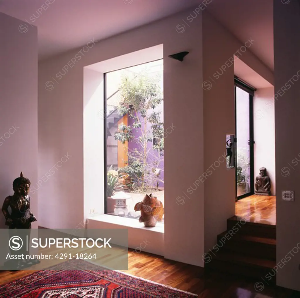 Oriental statue beside large window with view of courtyard in modern white hall