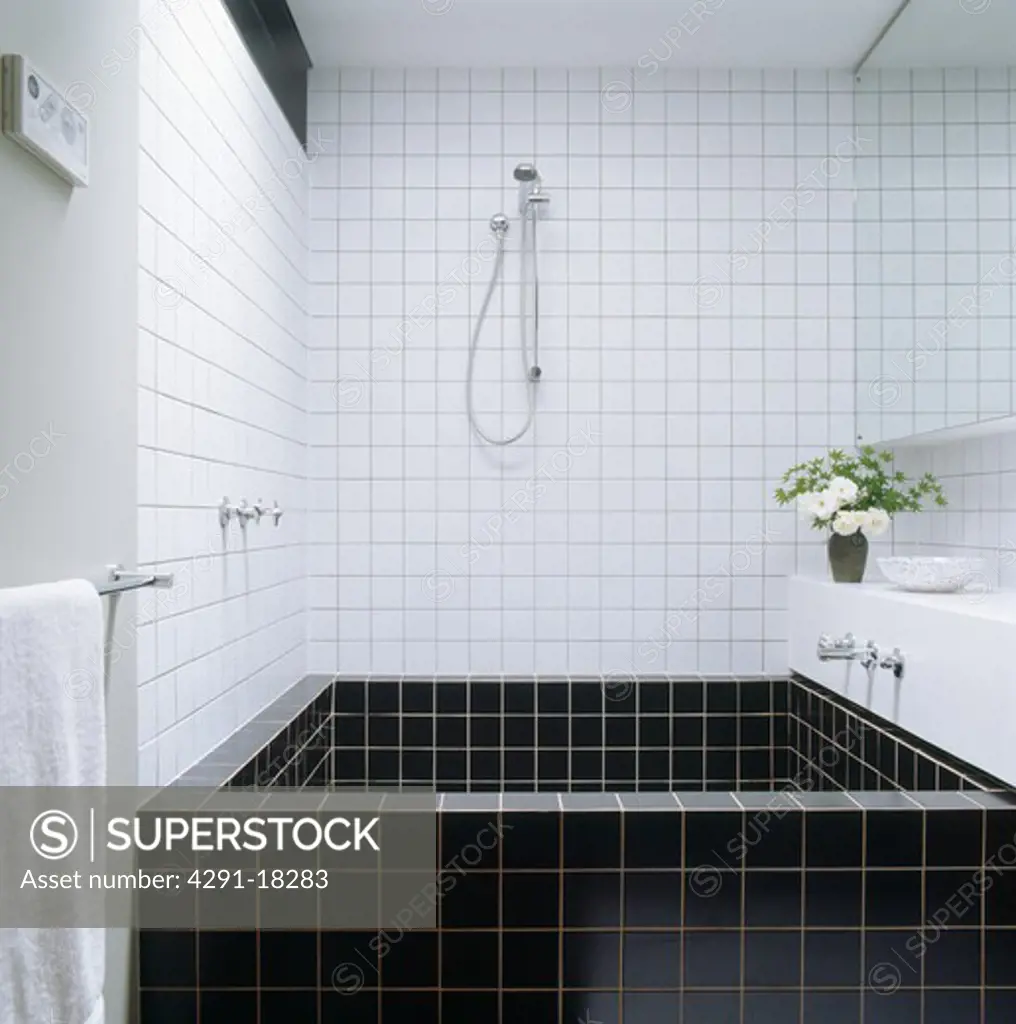 Shower above black tiled bath in modern white tiled bathroom