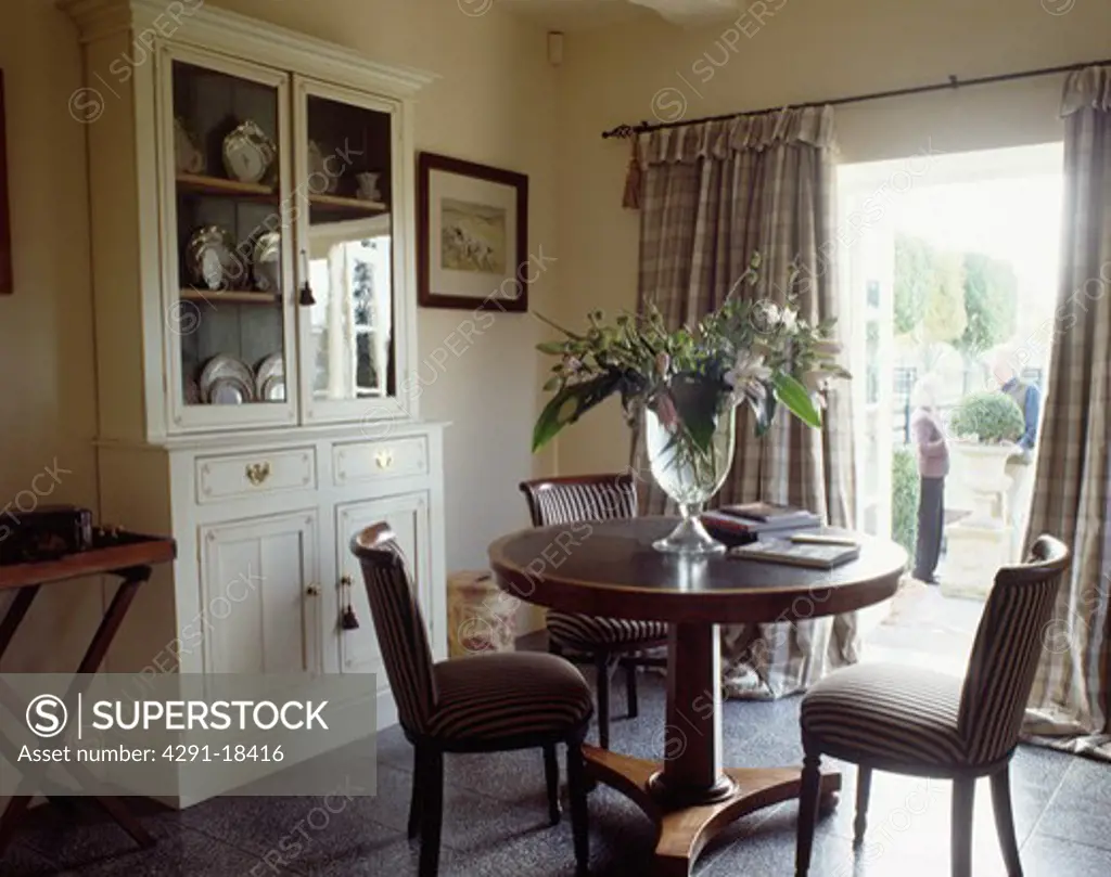 Mahogany antique pedestal table and striped upholstered chairs in dining room with white dresser and slate floor tiles