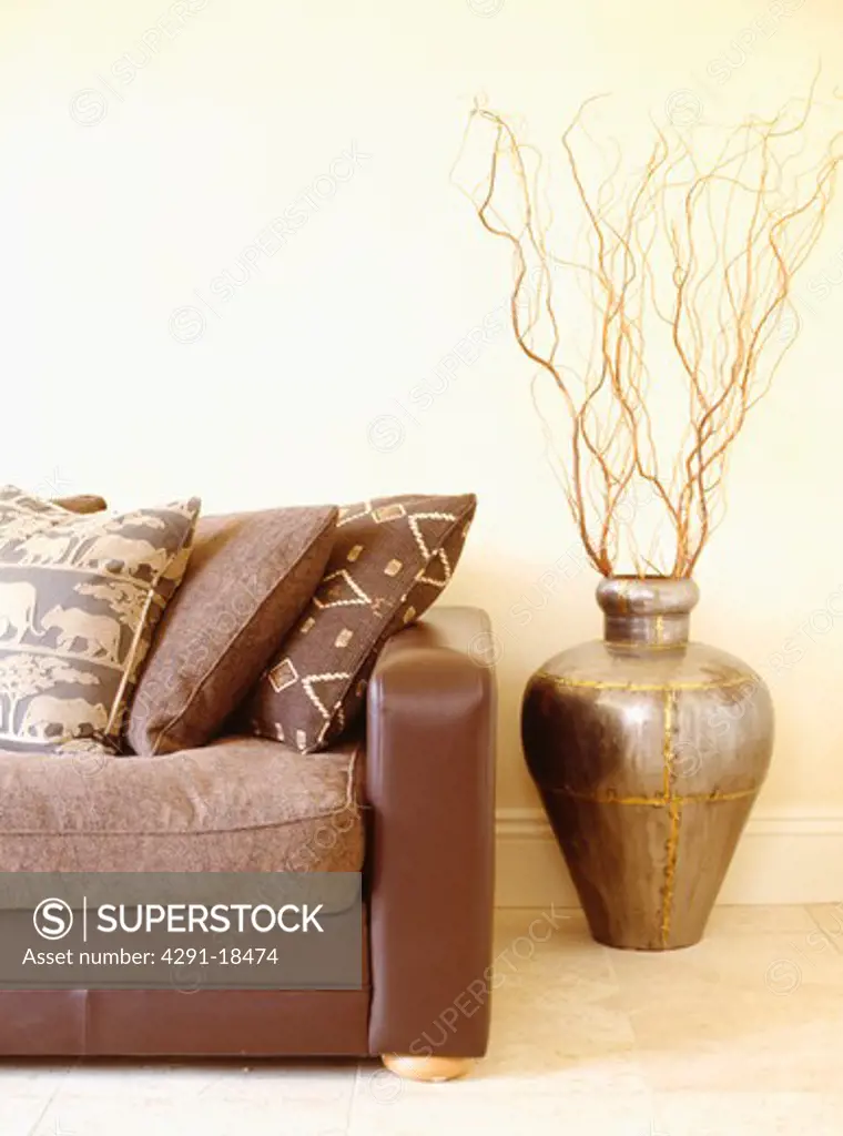 Ethnic-patterned cushions on brown leather sofa beside branches in Moroccan pot