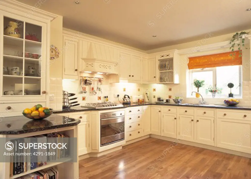 Cream fitted cupboards with black granite worktops in contemporary kitchen with wooden floor