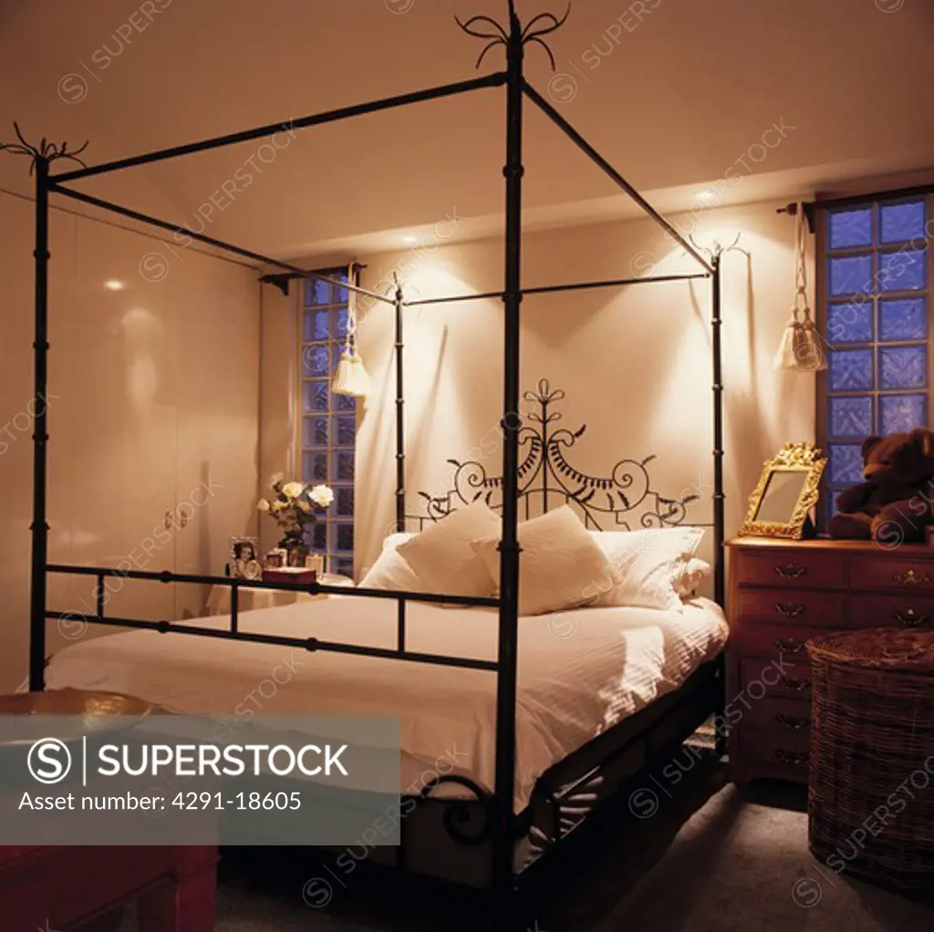 Modern black metal four-poster bed with white linen in modern bedroom with glass brick windows