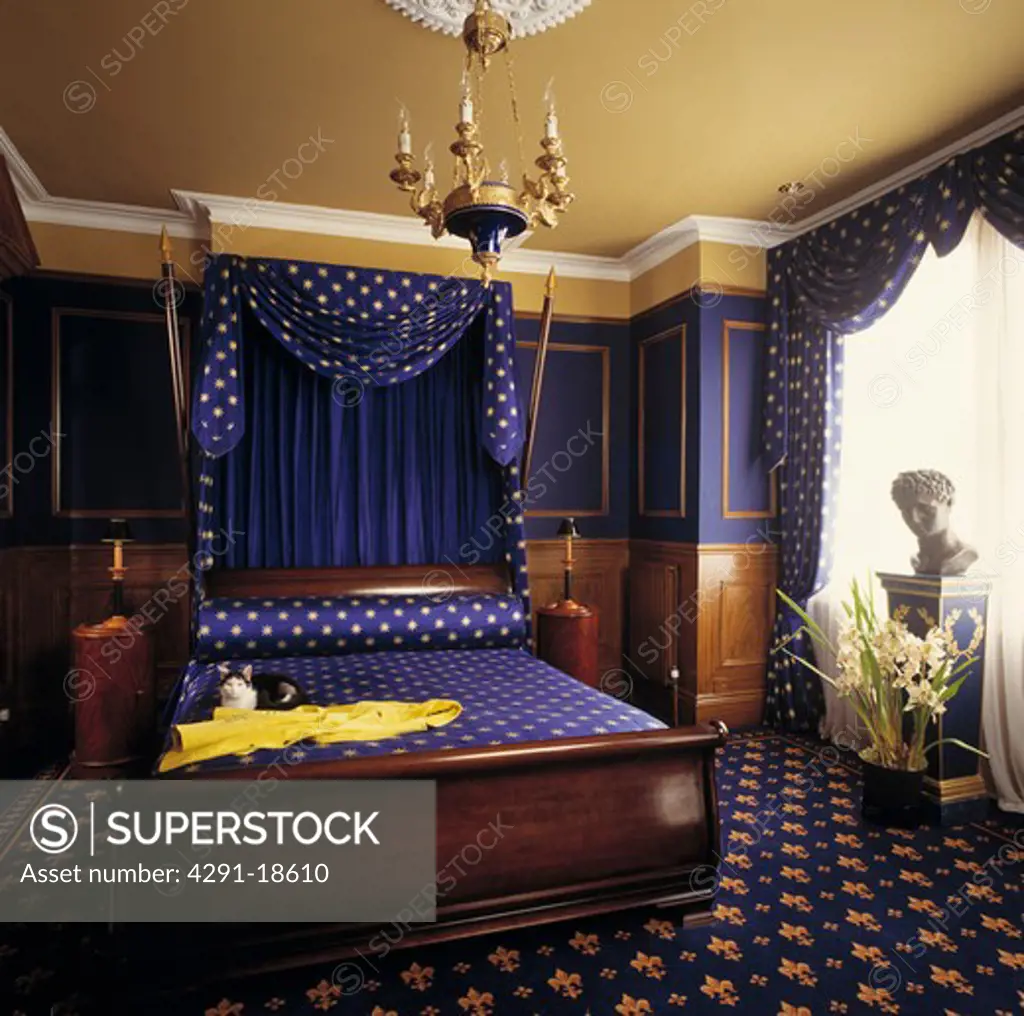 Blue and gold drapes and bedcover on mahogany half-tester bed in blue bedroom with gold and blue fleur-de-lis carpet