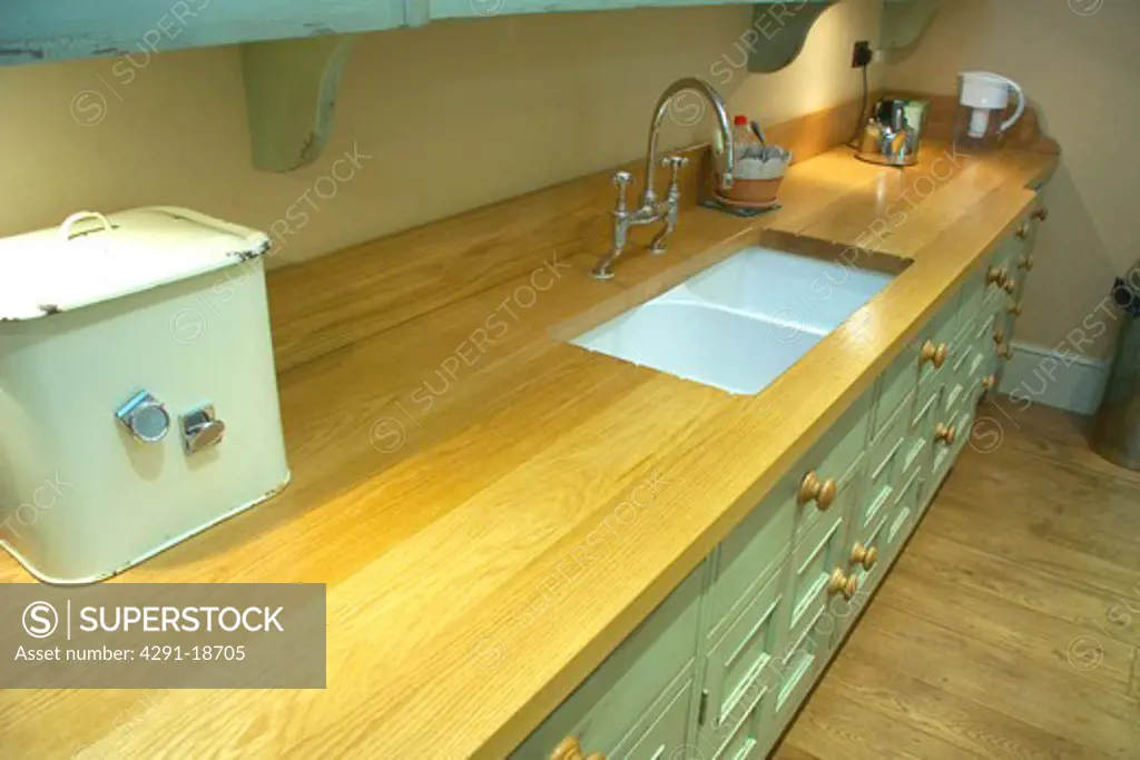 Pastel turquoise kitchen unit with enamel breadbin on wood worktop with underset double ceramic sinks