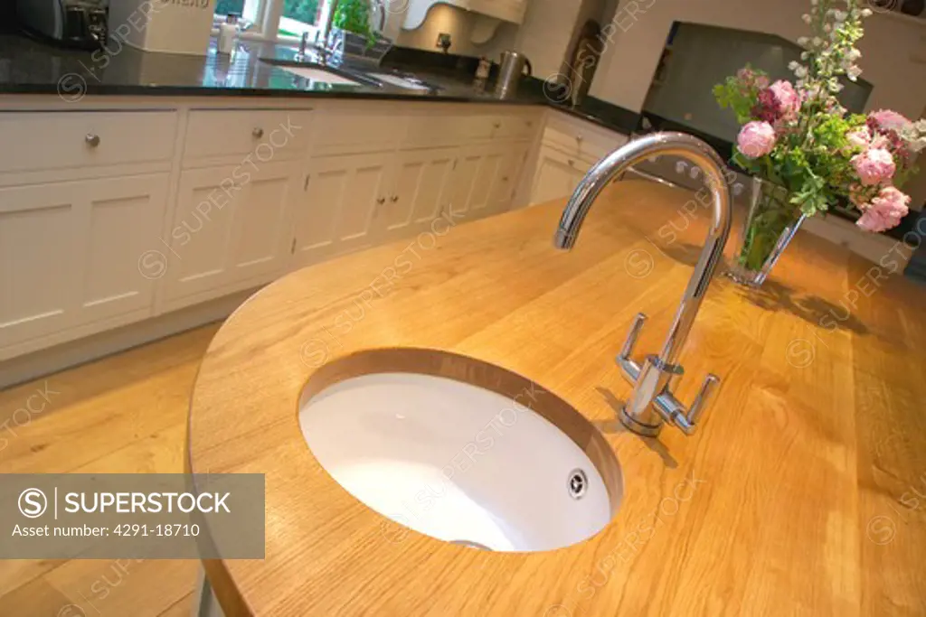 Close-up of chrome tap and white ceramic circular sink underset into wood worktop in modern kitchen