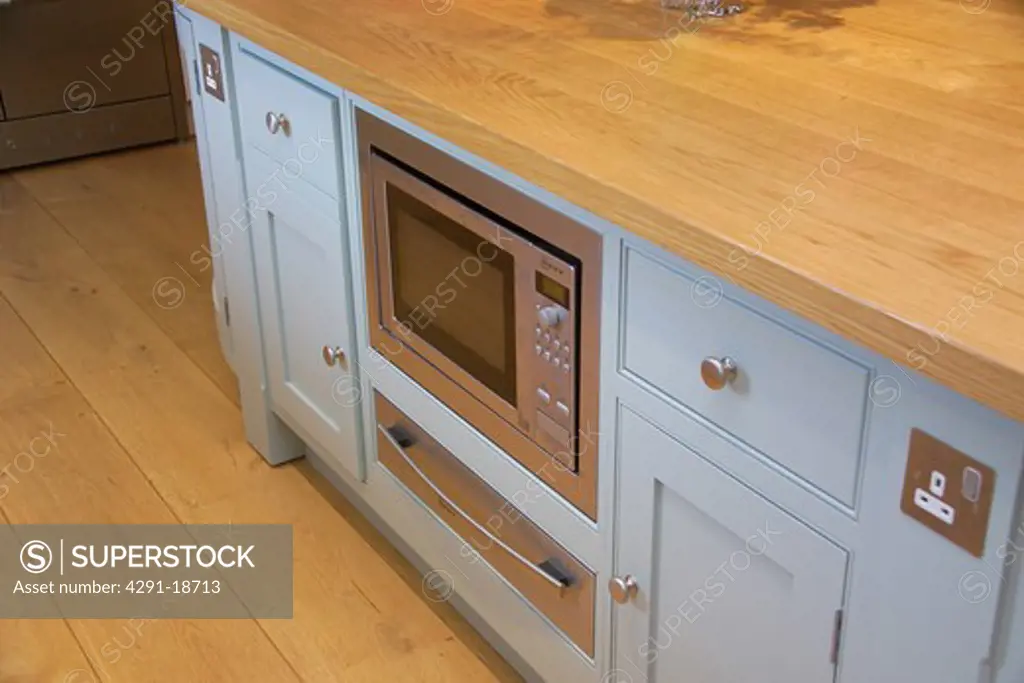 Close-up of pastel blue kitchen unit with fitted microwave oven and electric plug socket