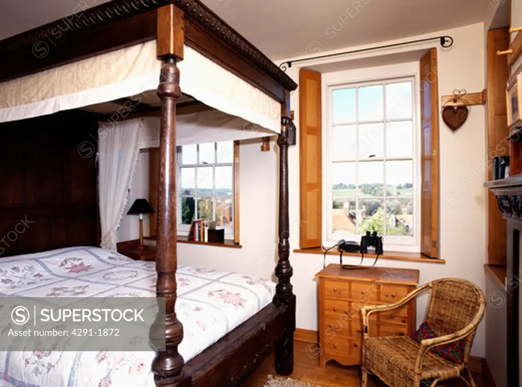 Antique wooden four-poster bed in traditional bedroom with wooden shutters and windows