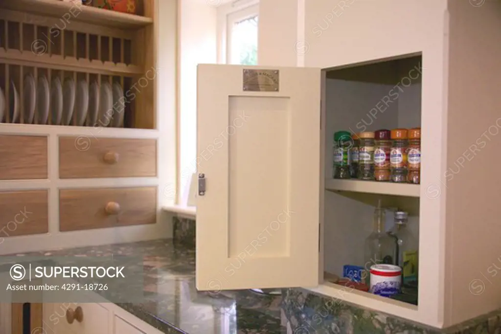 Close-up of storage cupboard with open door and spice jars on shelves