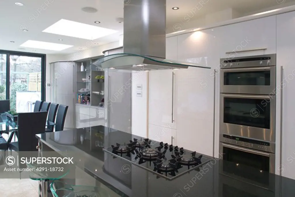 Extractor above hob set into island unit with granite worktop in modern white openplan kitchen and dining room