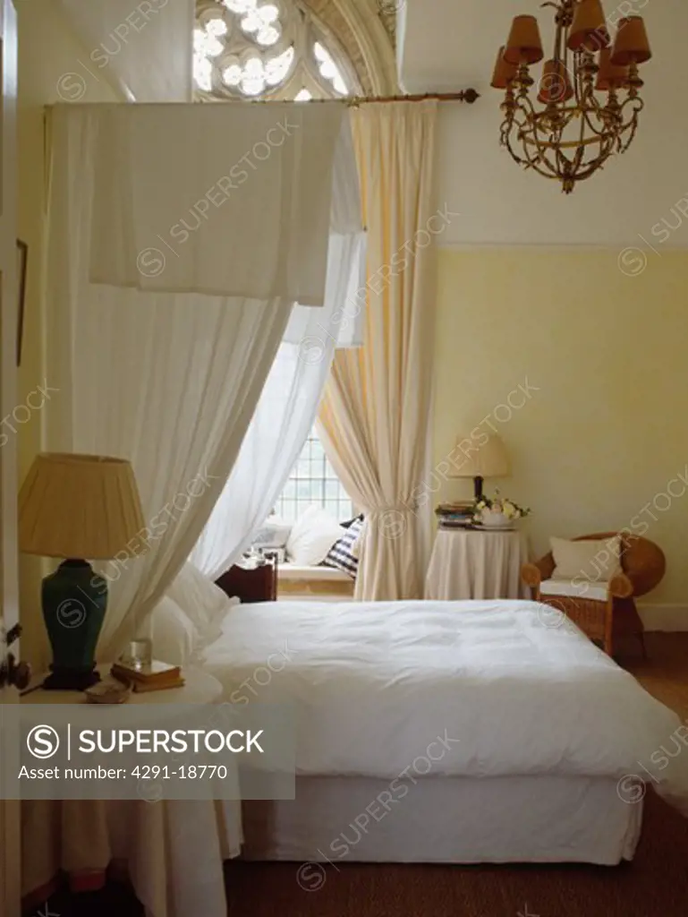 White curtains on half-tester bed in cream bedroom in converted church