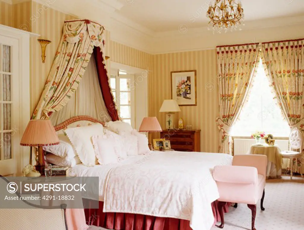 Coronet with floral drapes above bed in country bedroom with striped wallpaper