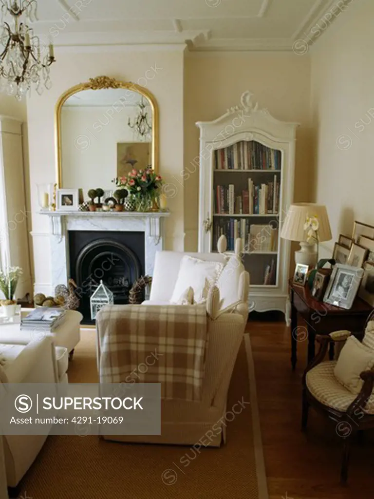 Gilt mirror above fireplace in traditional neutral living room with checked throw on sofa
