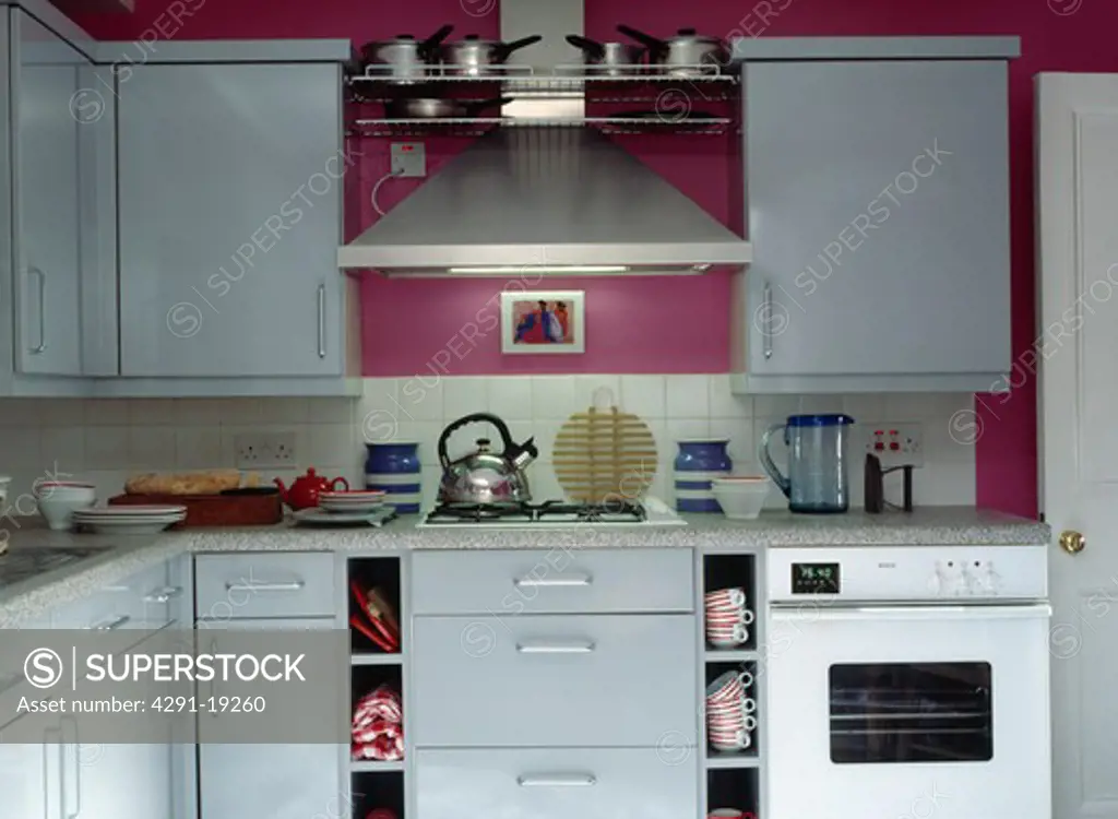 Stainless steel extractor above kettle on hob in small modern pink kitchen with fitted white units and white oven