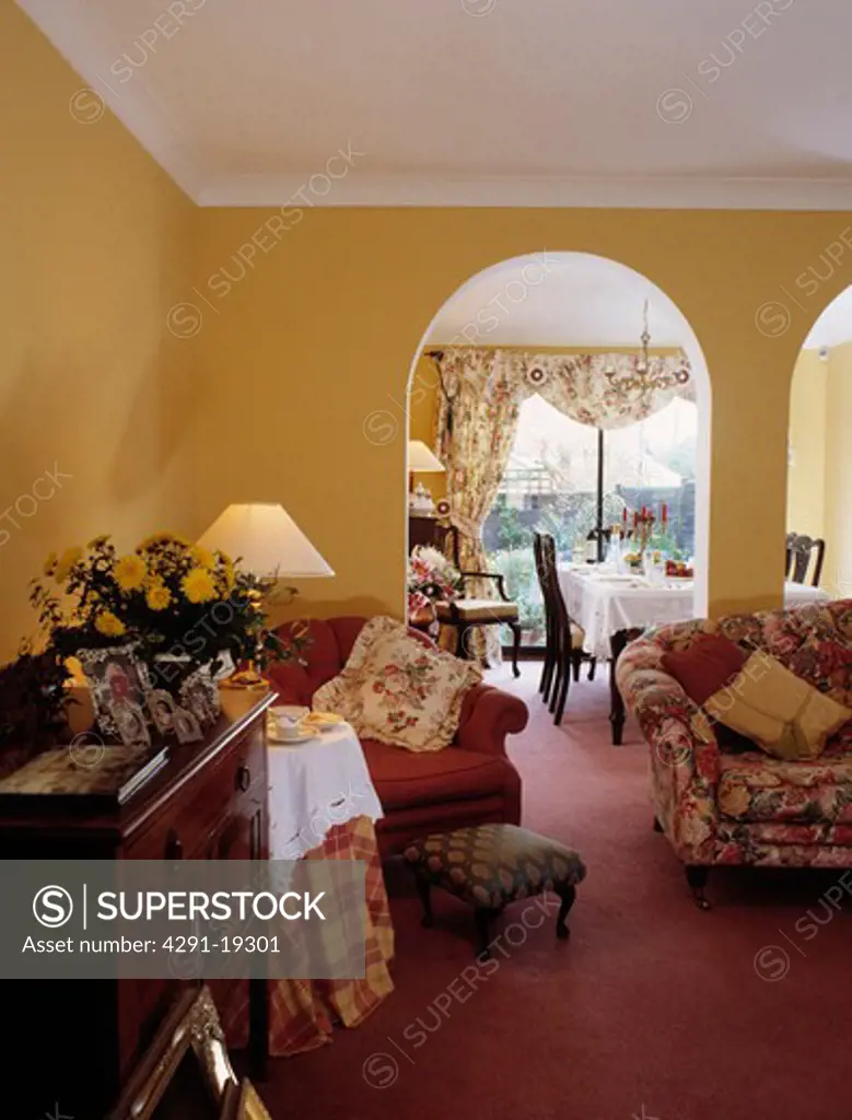 Lighted lamp on small table with cloth in yellow living room with comfortable armchairs in front of arches