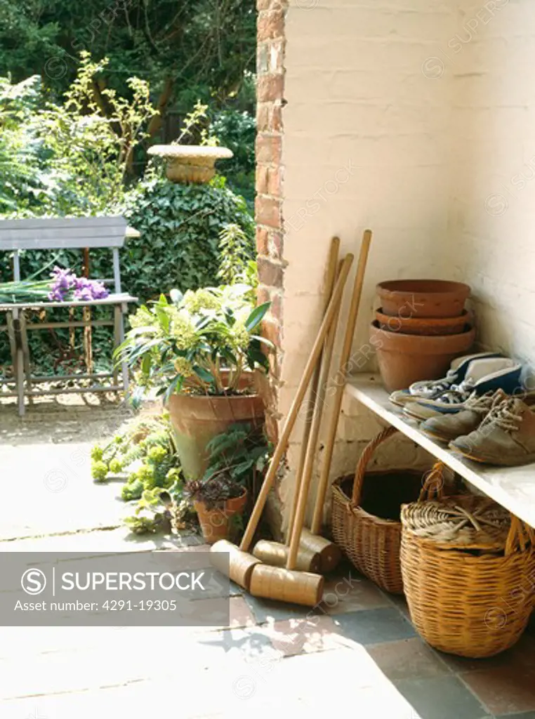 Baskets and croquet mallets with boots on shelf in porch with view of garden