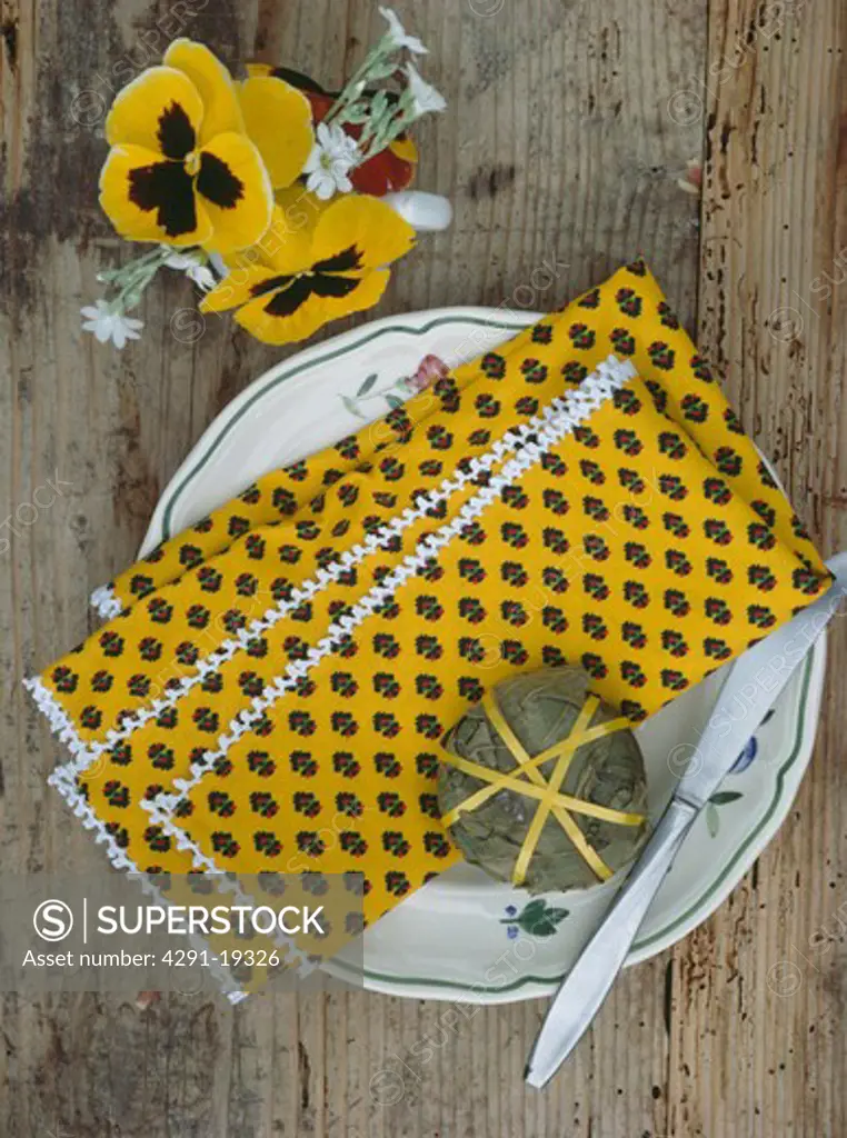 Yellow pansies beside plate with yellow Provencal napkin and stuffed vineleaf