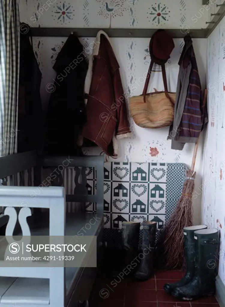 Clothes and bags hanging on peg-rail above Wellington boots in small cottage hall with pale blue wooden settle
