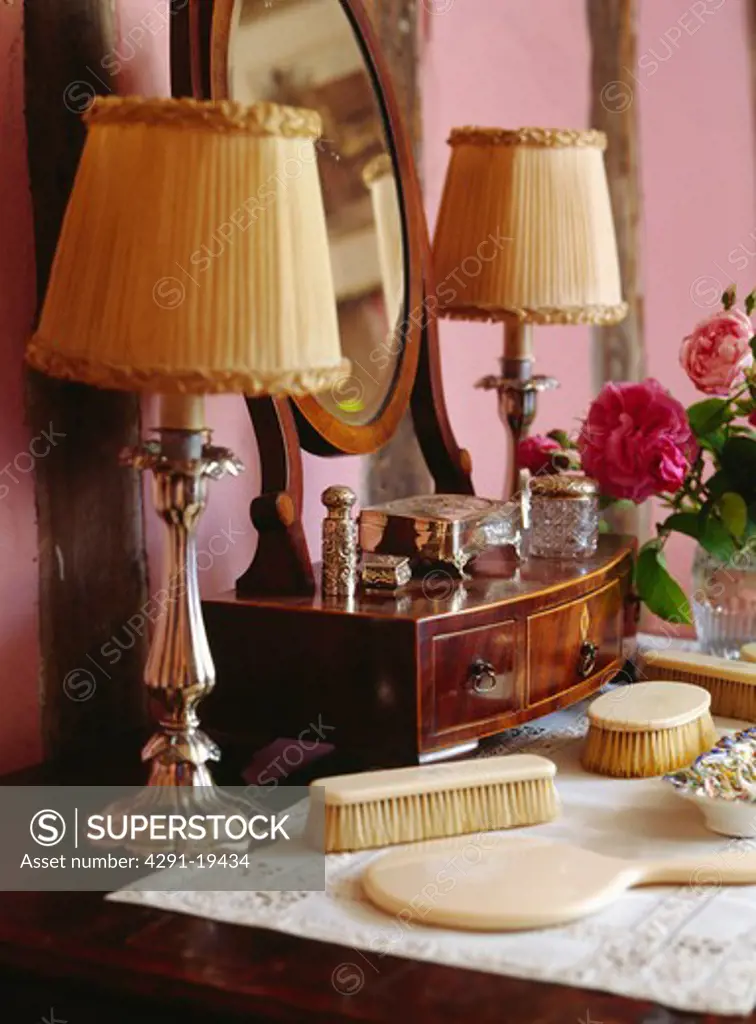 Close-up of metal lamps with cream ruched shades on dressing table with ivory brushes and hand-mirror