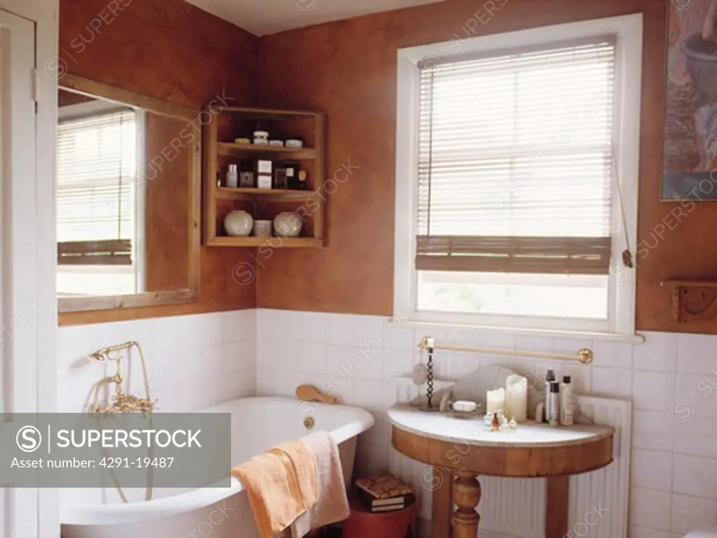 Brown sponge-effect walls above white tiles in bathroom with rolltop bath and small marble-topped antique table