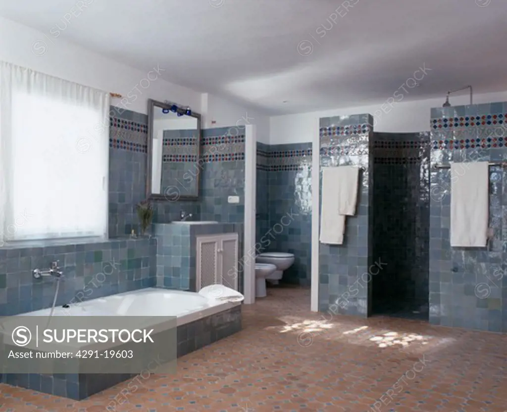 Sunken bath in blue tiled Spanish bathroom with tiled floor