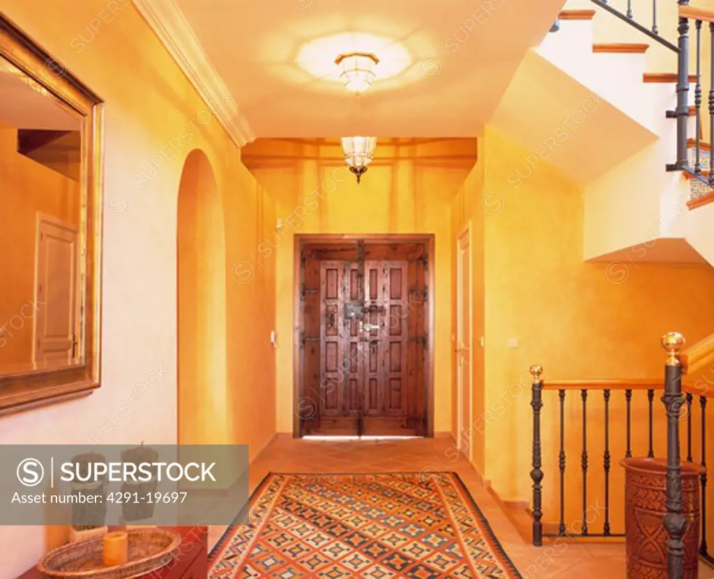 Lighted glass lantern above oriental rug in yellow Spanish hall with carved double doors