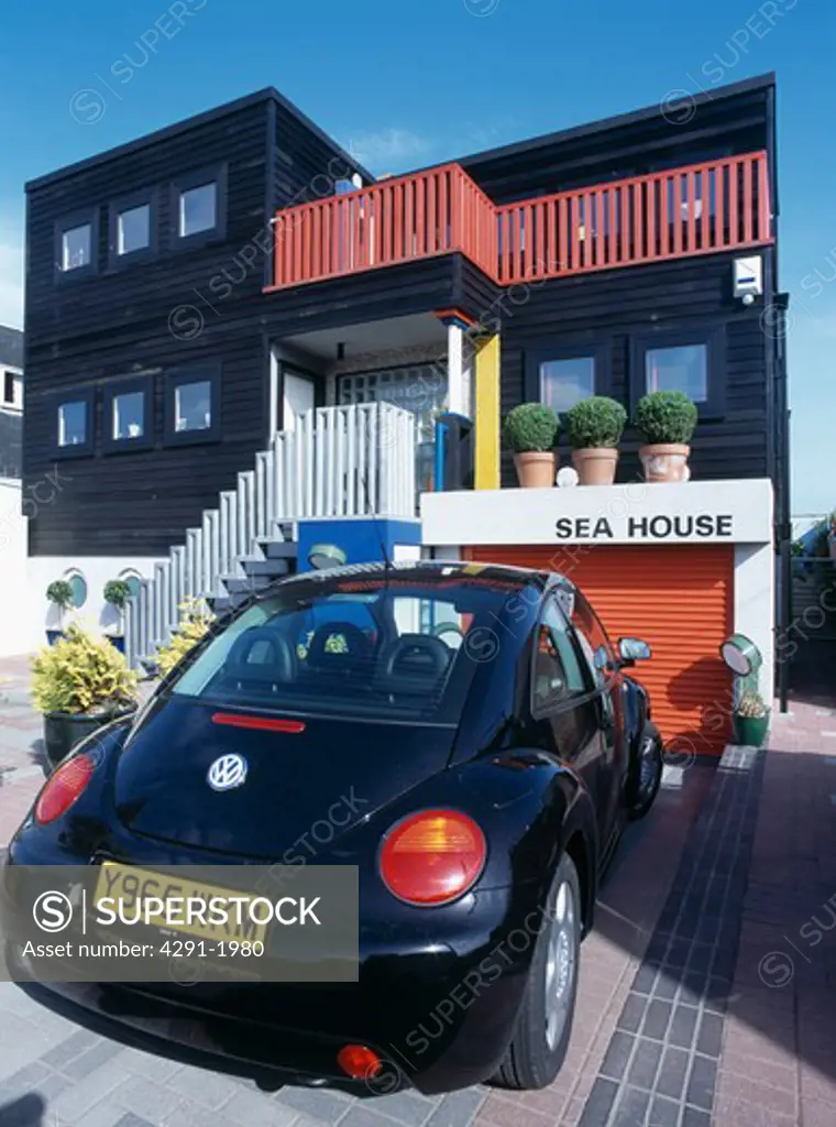 Black VW Beetle car outside modern black and red coastal house