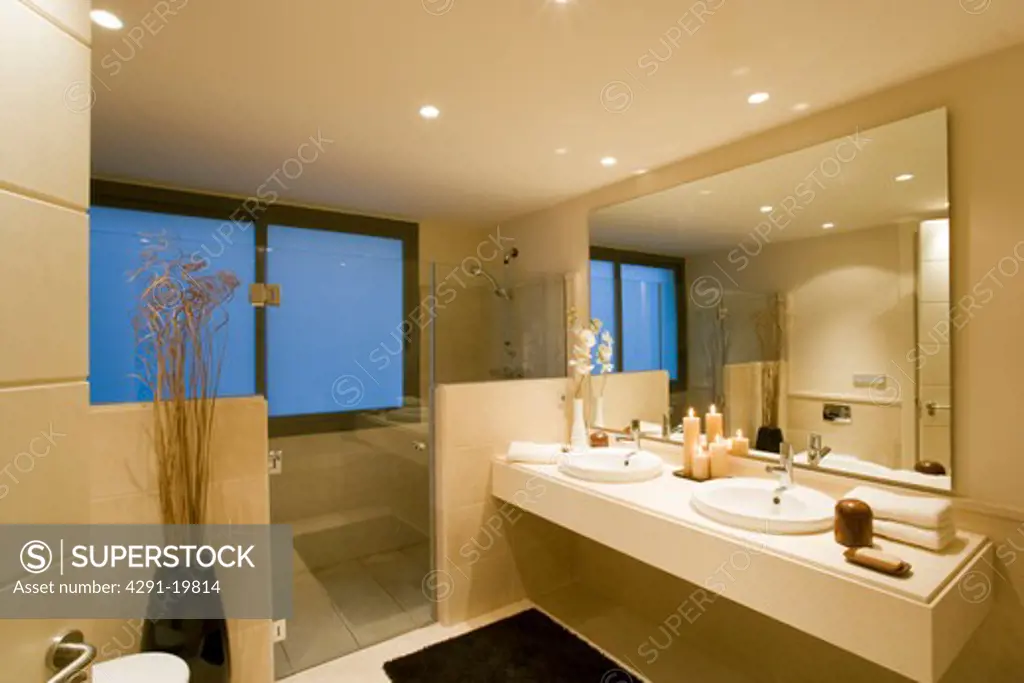 Glass doors to shower area in modern neutral bathroom with large mirror over double basins