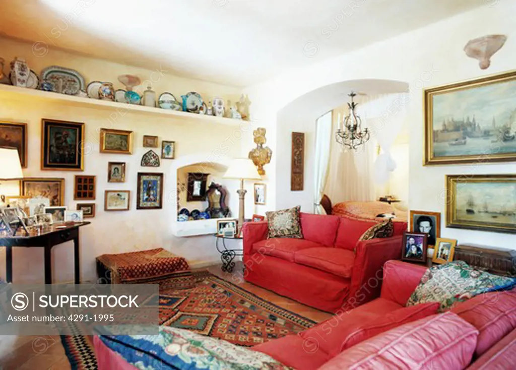 Groups of pictures on walls of Mallorcan living room with red sofas and oriental carpet