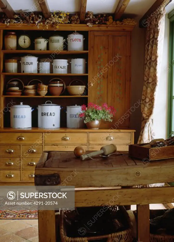 White enamel storage canisters on antique pine dresser in country kitchen with old wooden butcher's block
