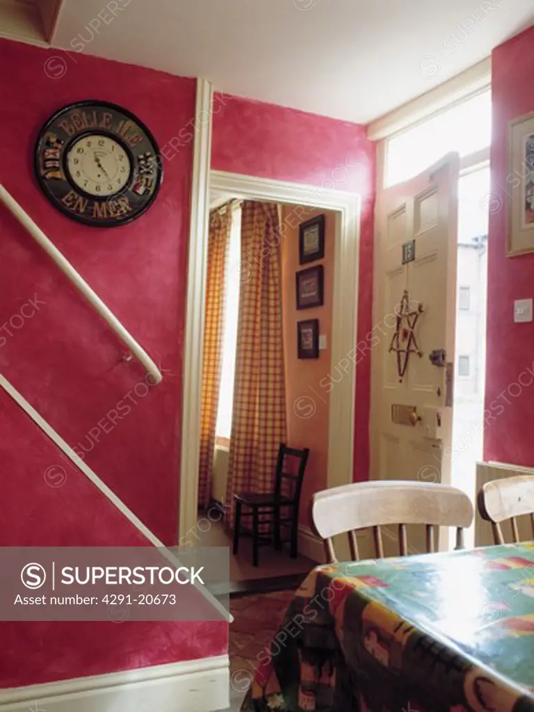 Circular clock on wall in pink cottage hall with dining chairs and table