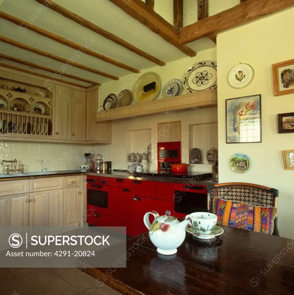 Teapot and cup on wooden table in country kitchen with red Aga