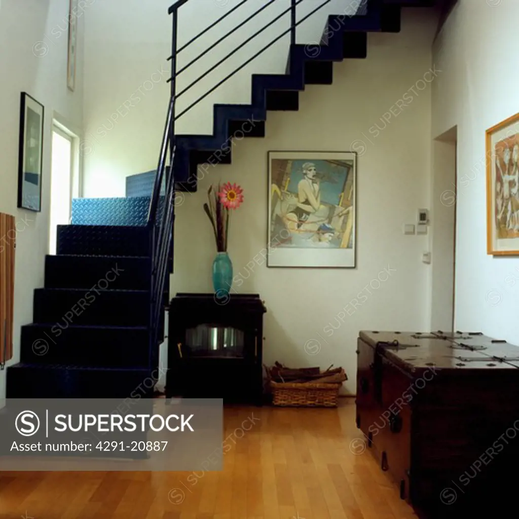 Large wooden chest and black iron stove in modern hall with wooden flooring and black metal staircase