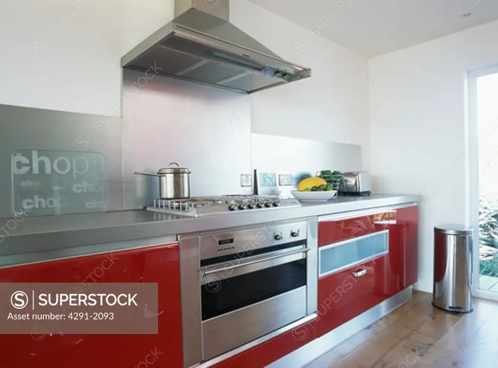 Steel extractor above range oven in large white kitchen with red fitted units