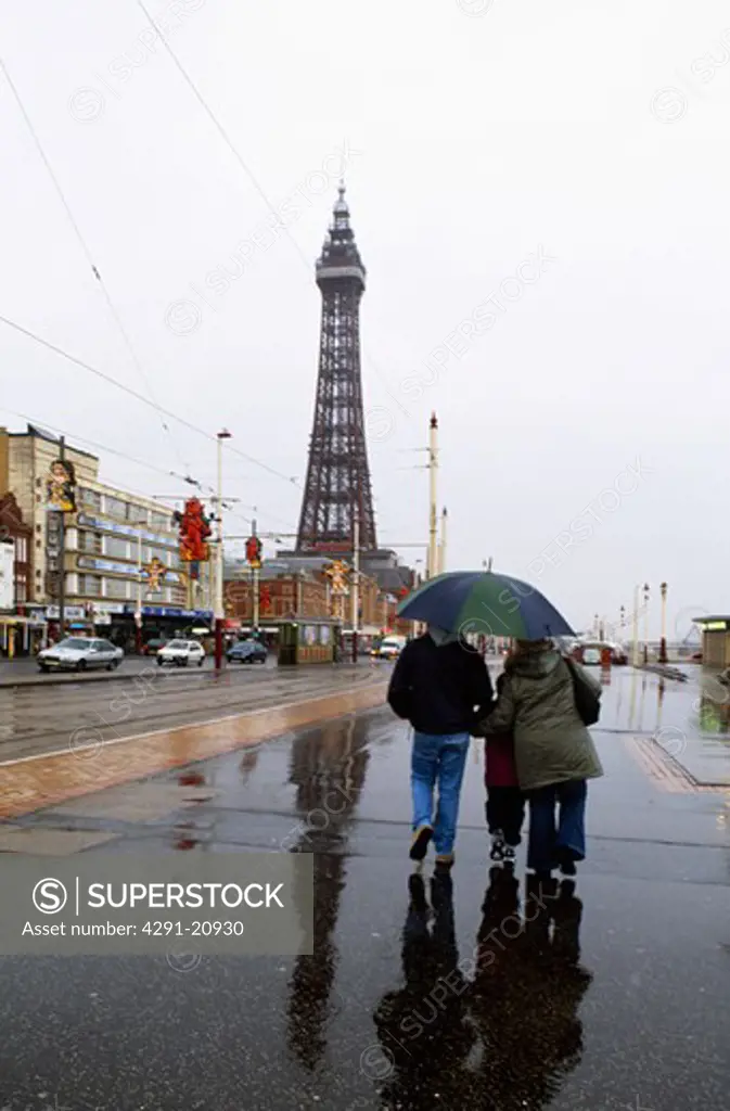 People walking beneath umbrella in the rain at Blackpool with Blackpool Tower in the background