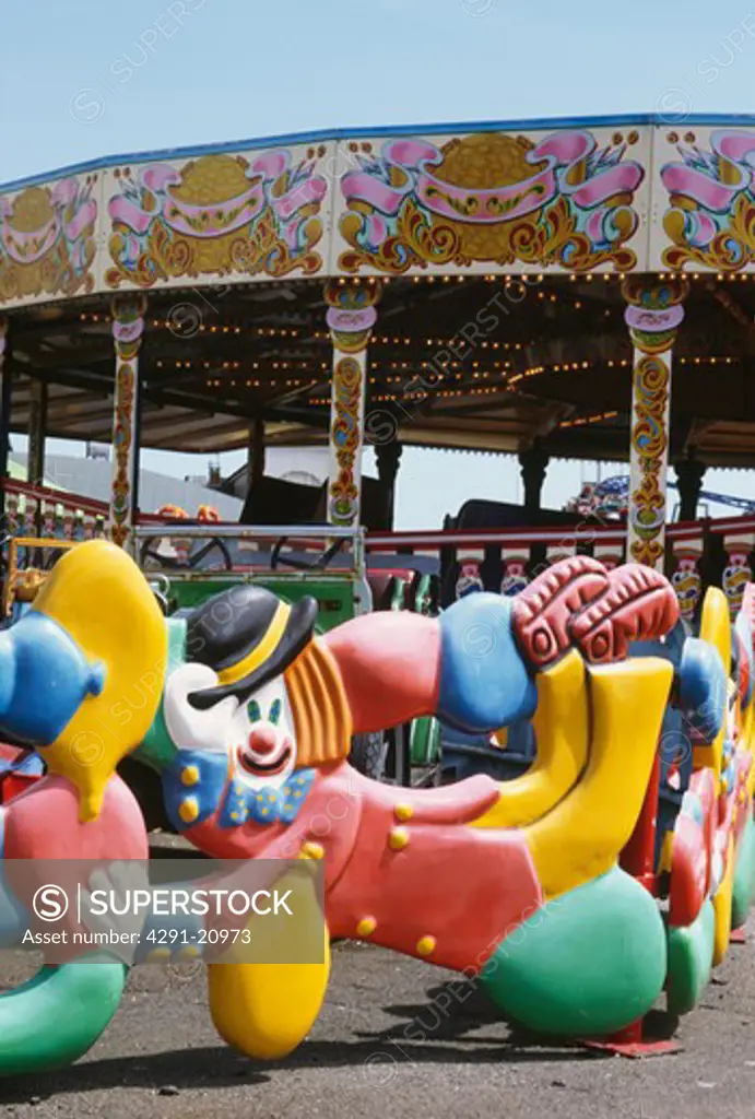 Large brightly coloured plastic clown figures in front of fairground carousel at Folkestone in Kent